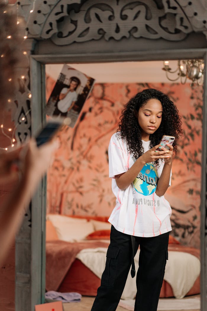 A young woman is focused on her phone, standing in a creatively designed room, showcasing modern youth culture.