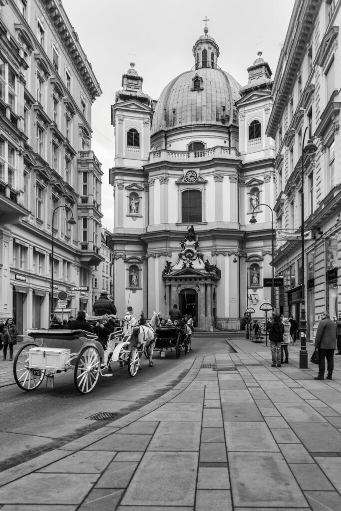 Black and white urban photo of a cathedral with horse carriages, capturing classic city architecture.